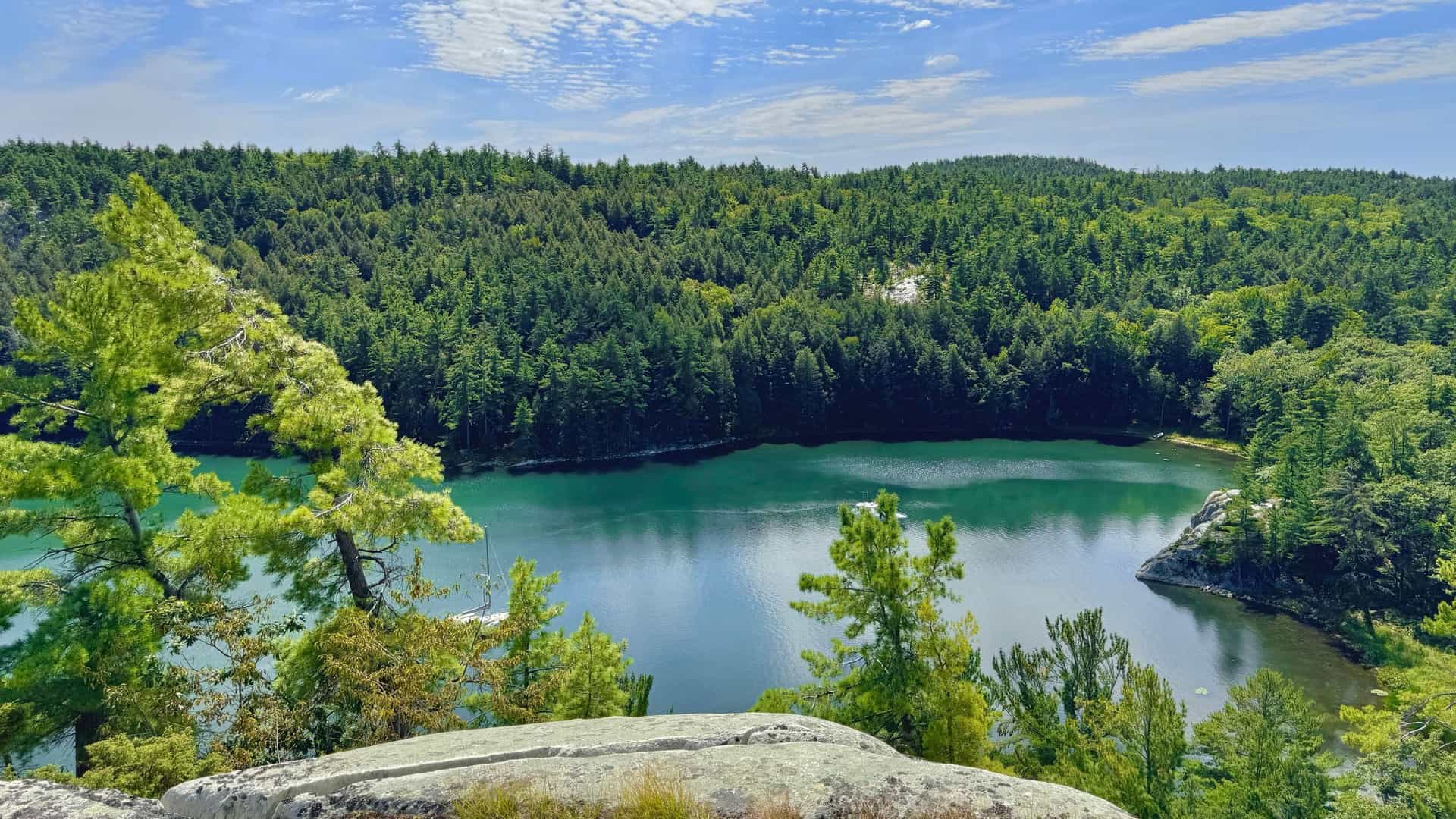 A high-angle view of a serene cove surrounded by dense, green forests and rocky outcroppings on the Benjamin Islands, with a boat anchored in the calm, turquoise water.