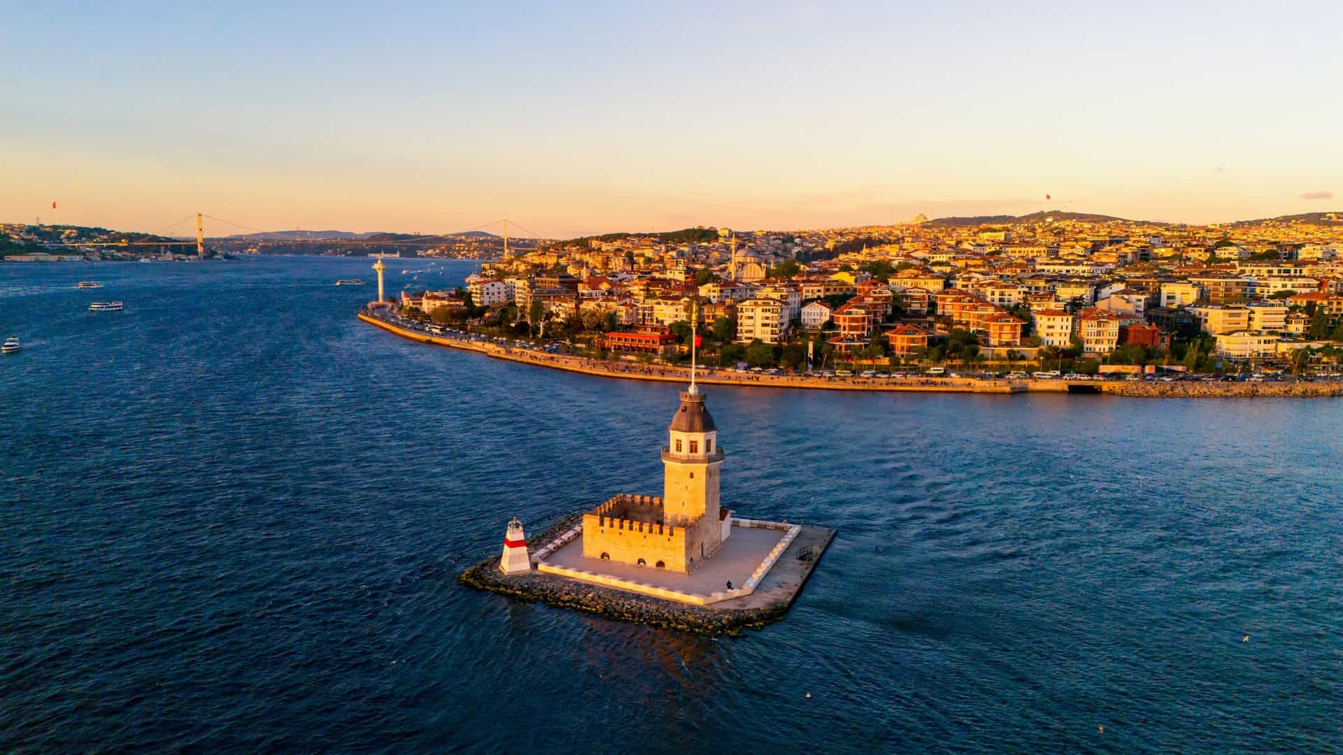 An aerial view of the Maiden's Tower (Kız Kulesi) on a small islet in the Bosphorus Strait, Istanbul, Turkey, under a warm sunset glow.