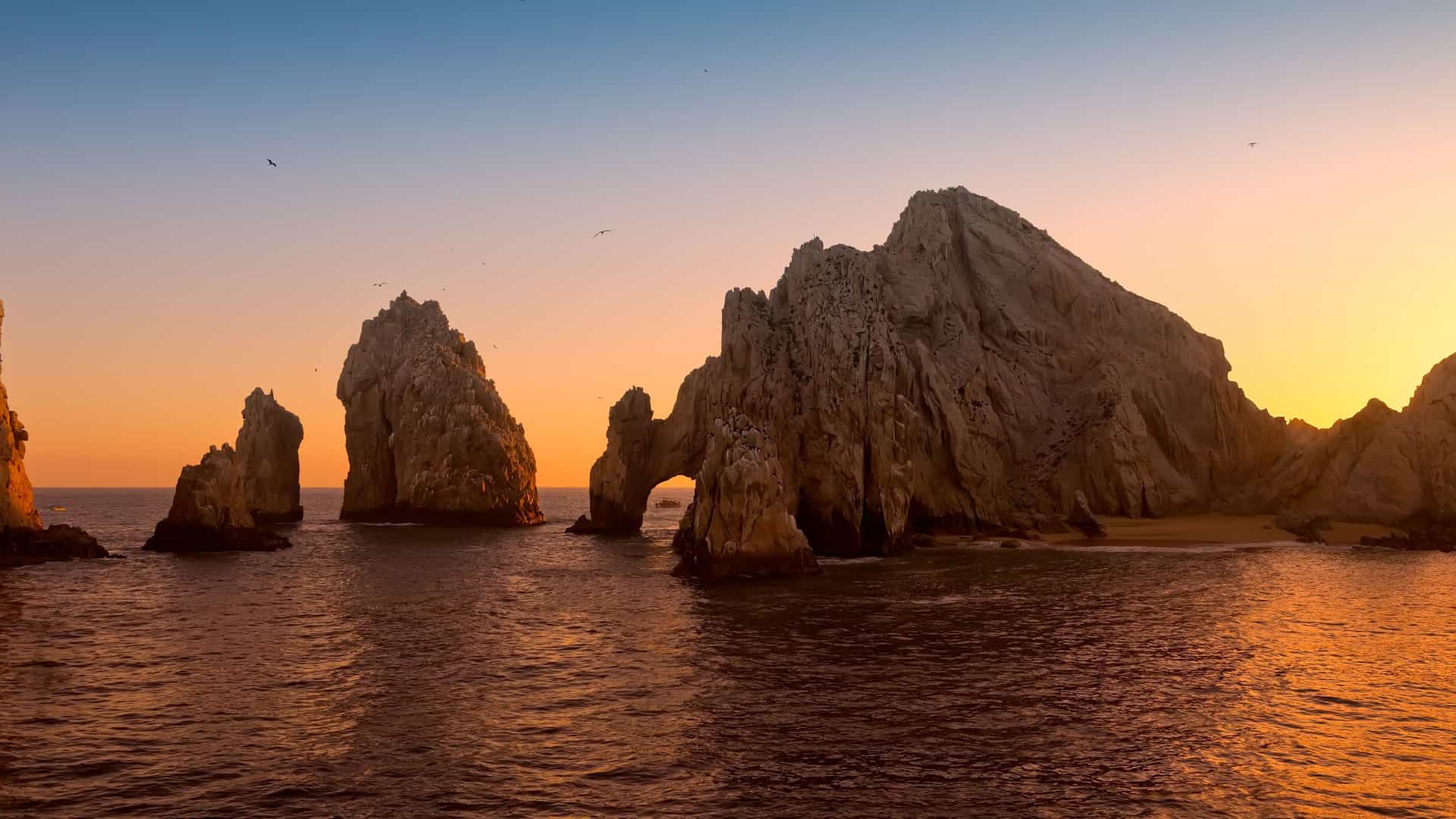 A scenic sunset over the iconic rock formations of Land's End, including El Arco, a major landmark of Cabo San Lucas, Mexico.