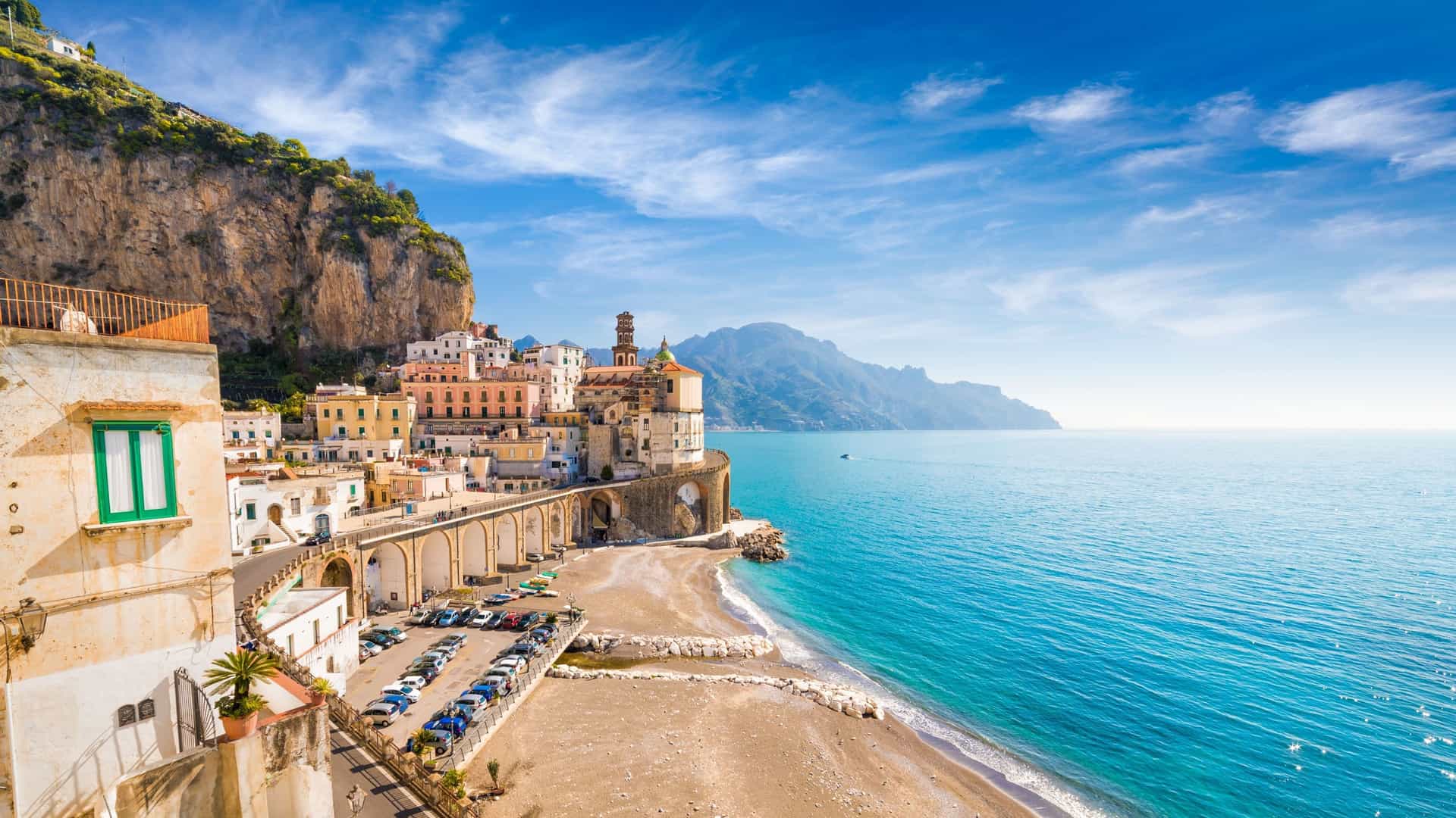 A scenic view of Capri, Italy, featuring a cliffside town with colorful buildings, a small beach, and the sparkling turquoise waters of the Mediterranean Sea.