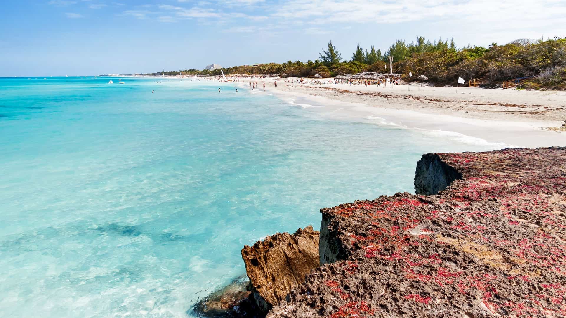 Tourists relaxing on Varadero Beach with white sand and turquoise water in Matanzas Province, Cuba. Rugged limestone foreground.
