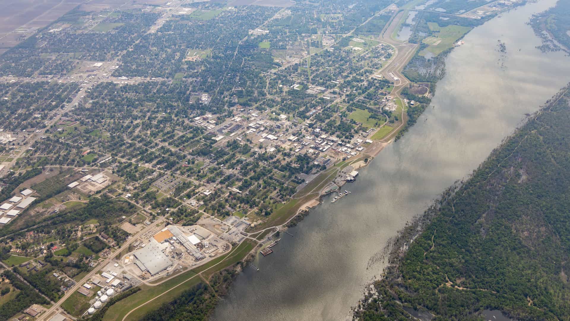 "An aerial view of Greenwood, Mississippi, showing the city's grid-like street layout, the Yazoo River with its curving banks, and the surrounding green landscape and farmland.  "