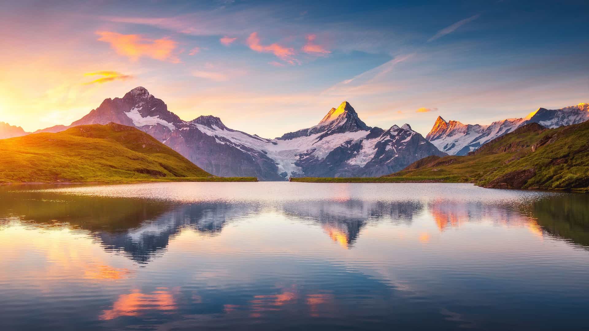 A stunning view of the snow-capped Bernese Alps reflecting on the tranquil Bachalpsee lake near Grindelwald, Switzerland, during a beautiful sunrise or sunset.