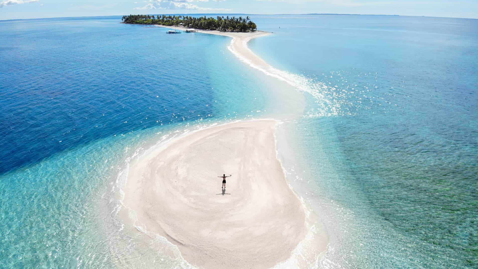 An aerial view of the brilliant white sandbar extending from Kalanggaman Island, The Philippines, surrounded by clear blue water.