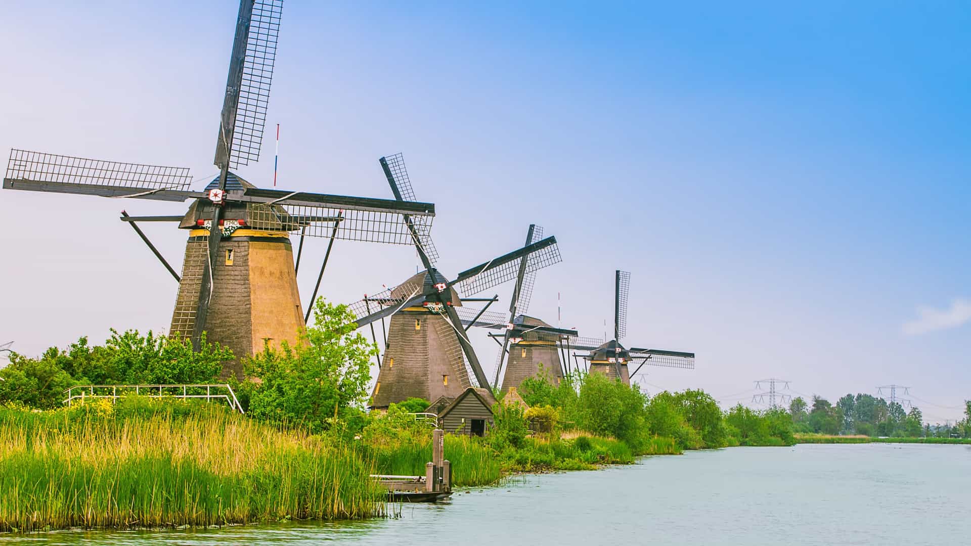 A row of historic thatched-roof windmills stand along the tranquil canal at Kinderdijk, Netherlands, a UNESCO World Heritage site and popular tourist destination.