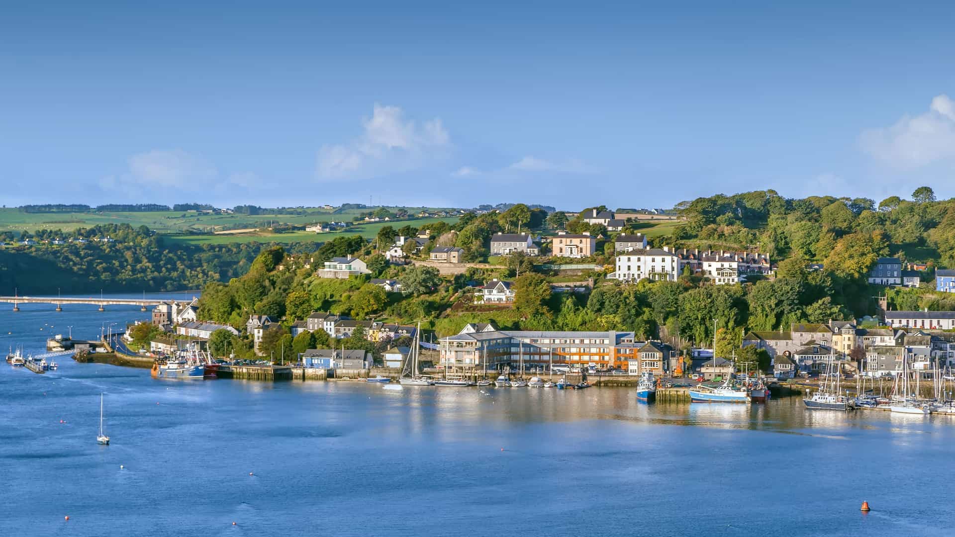 "A beautiful harbor shot of the coastal town of Kinsale, Ireland, with colorful buildings and houses lining the steep hills overlooking the calm water, with boats and yachts moored in the marina.  "
