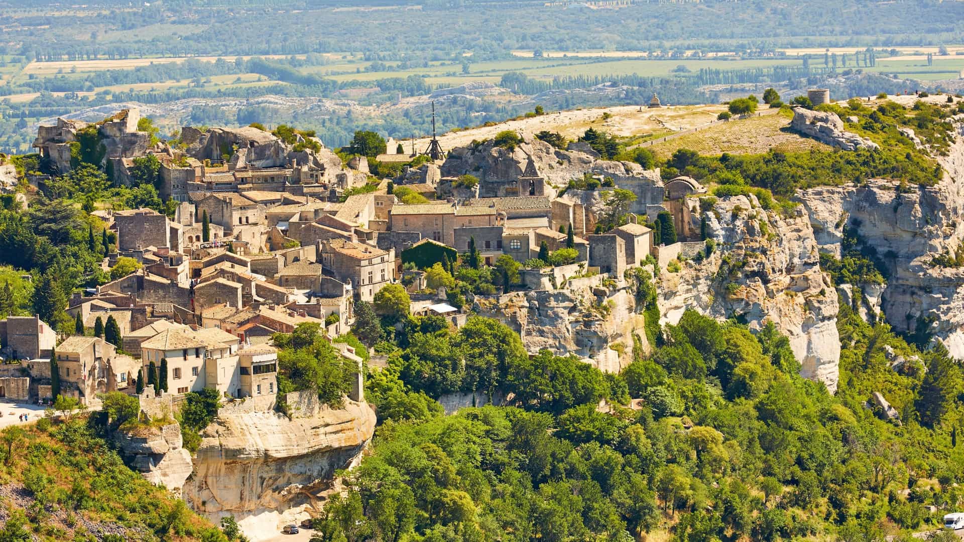 An aerial view of the historic village of Les Baux-de-Provence, a picturesque French commune built into the rock face of a clifftop with a beautiful landscape in the background.