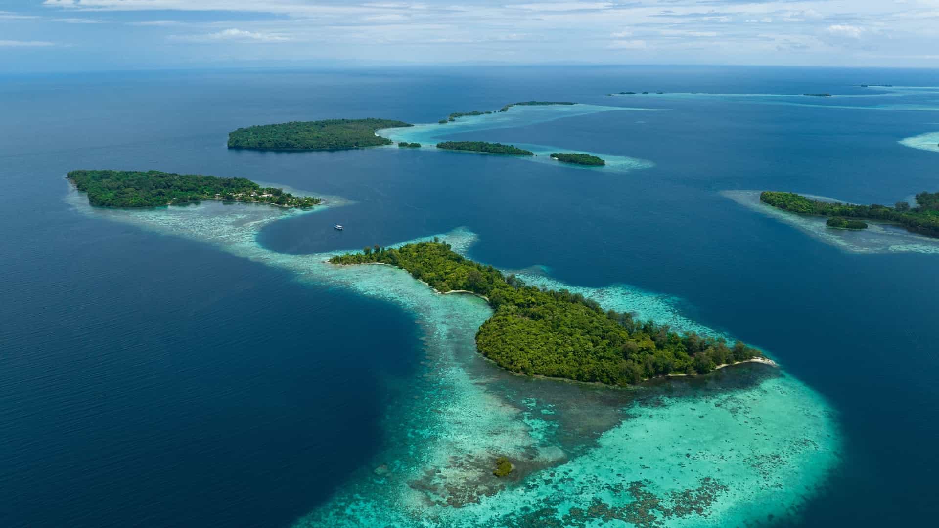 An aerial view of lush, green tropical islands surrounded by deep blue ocean and bright turquoise coral reefs at Lumalihe Island.