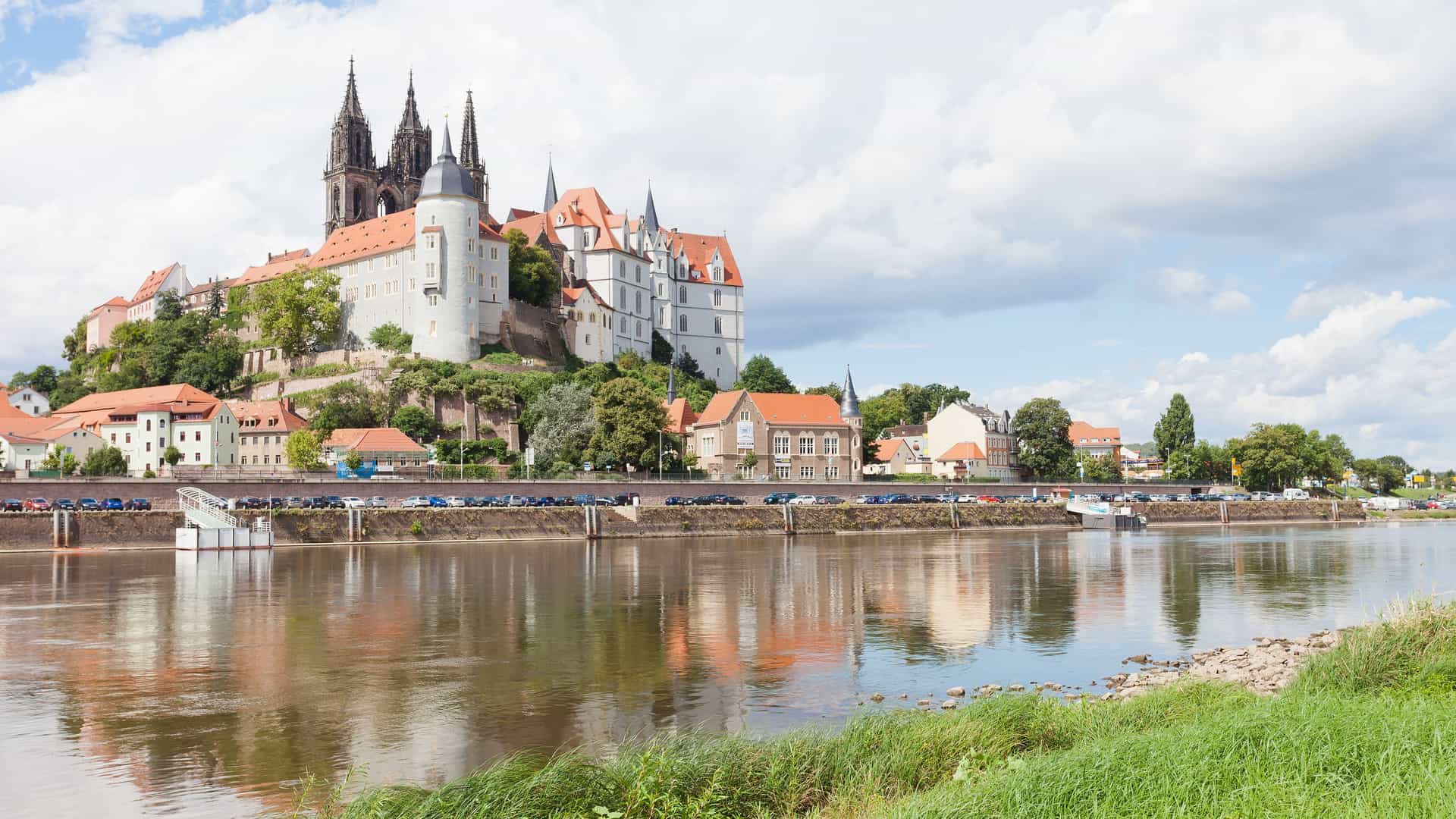 A wide-angle view of the historic Albrechtsburg Castle and the Meissen Cathedral, located on a hill overlooking the Elbe River in Meissen, Germany.