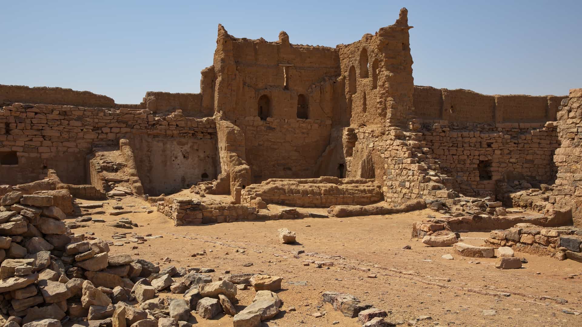The vast, sun-bleached ruins of the stone and mud-brick Monastery of St. Simeon stand against a clear sky near Aswan, Egypt.