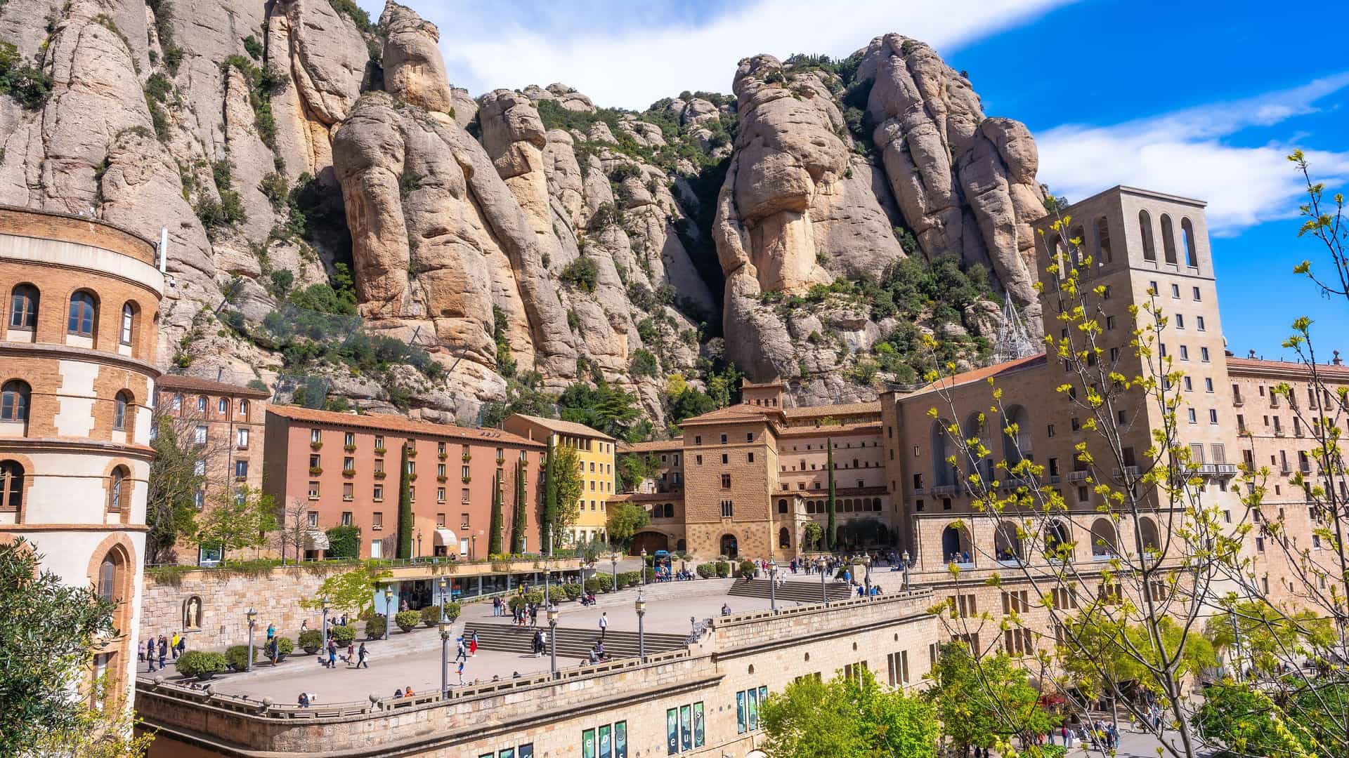 "A stunning view of the Santa Maria de Montserrat Abbey in Spain, with its historic buildings nestled against the dramatic, rocky Montserrat mountain range.  "