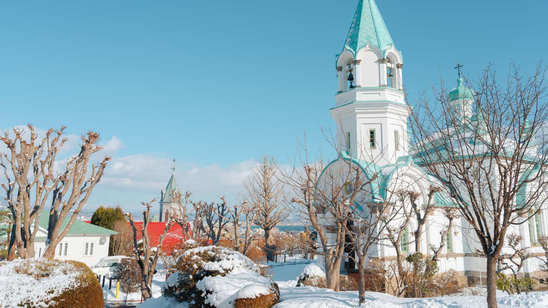 The white and turquoise onion domes of the Hakodate Orthodox Church are visible in a snowy landscape in Motomachi, Japan.