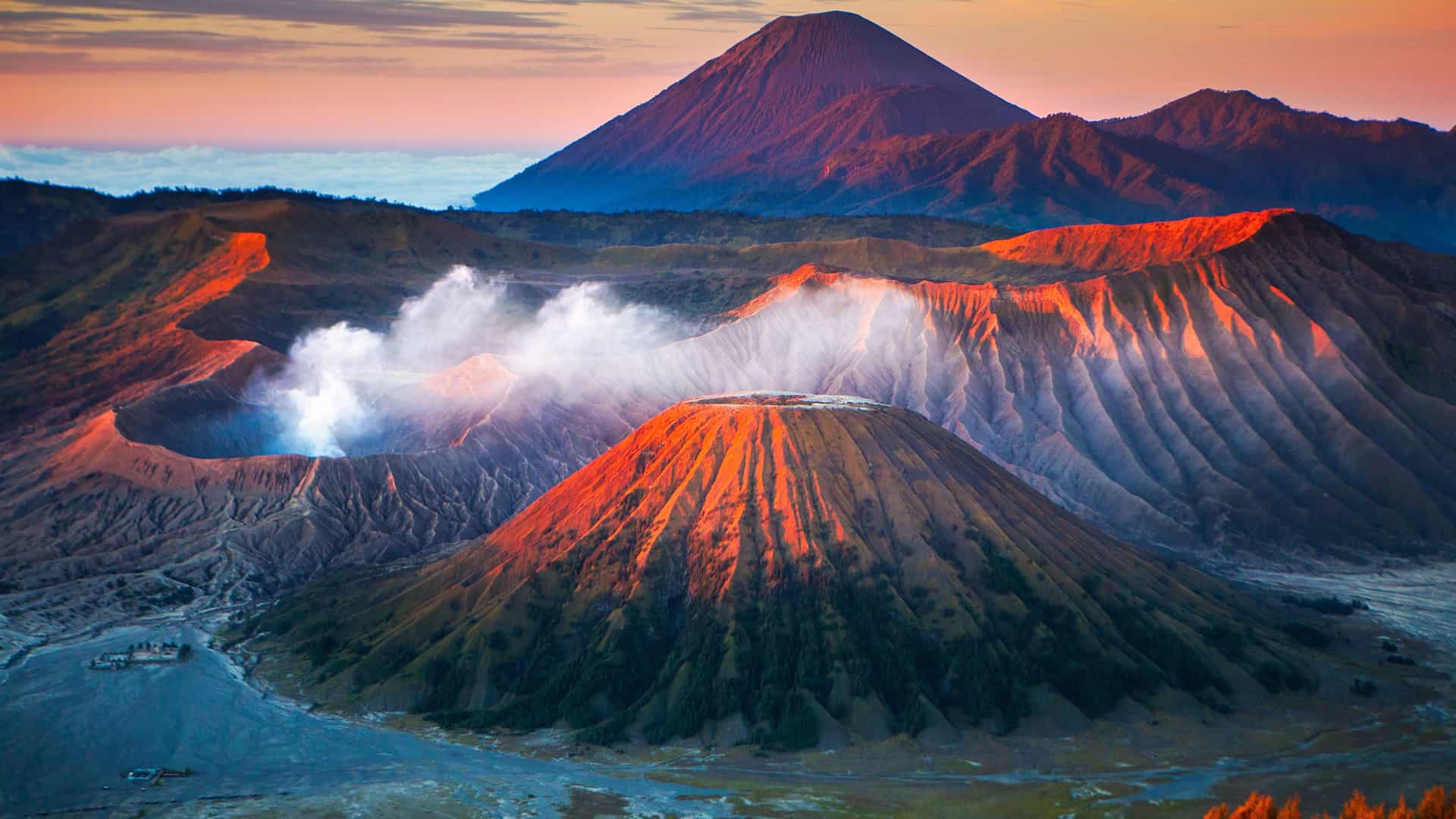 "An aerial panoramic sunrise view of the volcanic landscape in East Java, Indonesia, showcasing the smoking Mount Bromo crater and the surrounding Tengger caldera.  "