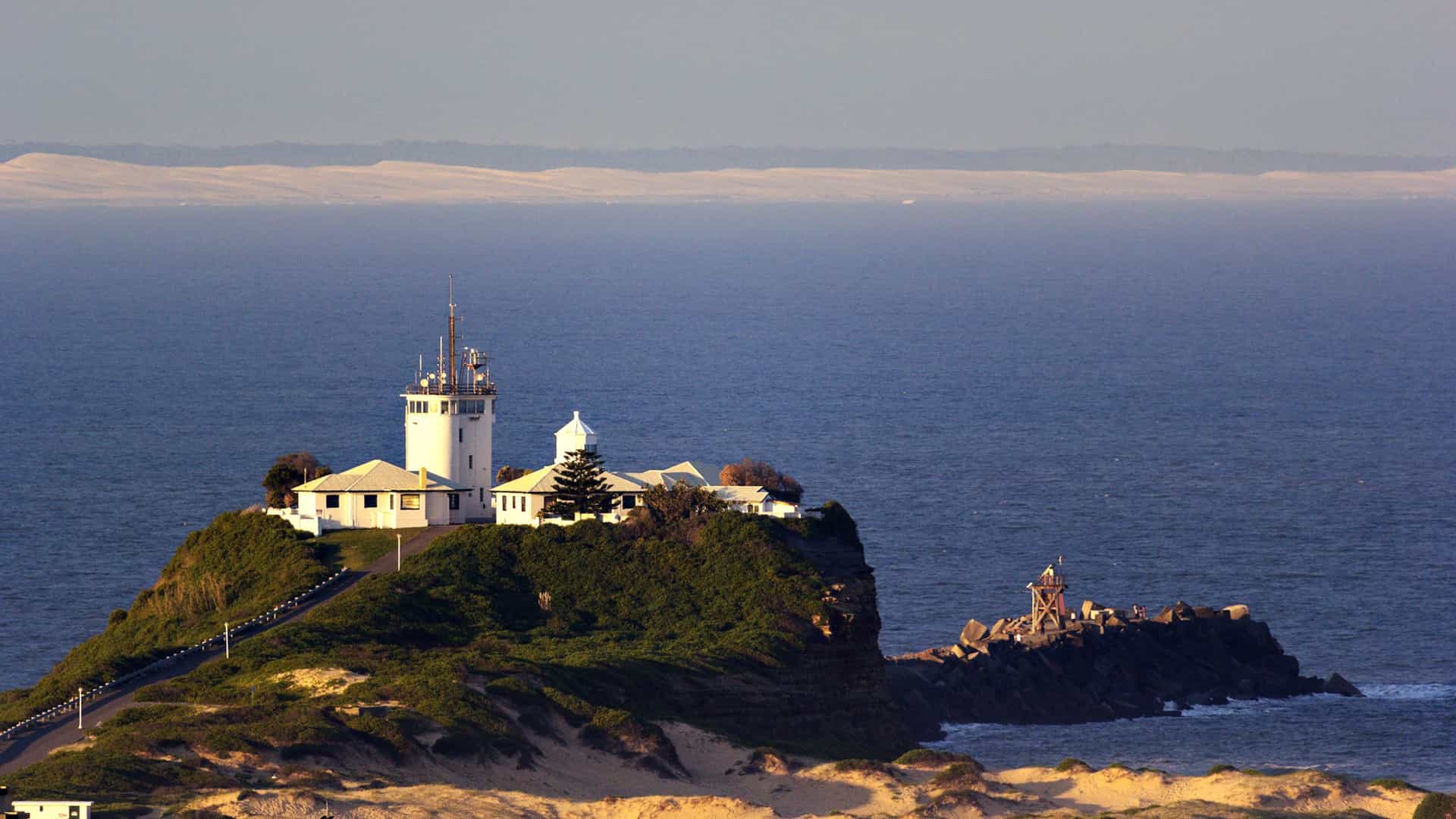 A stunning view of Nobbys Head Lighthouse and Signal Station in Newcastle, NSW, Australia, perched on a headland overlooking the deep blue Pacific Ocean.
