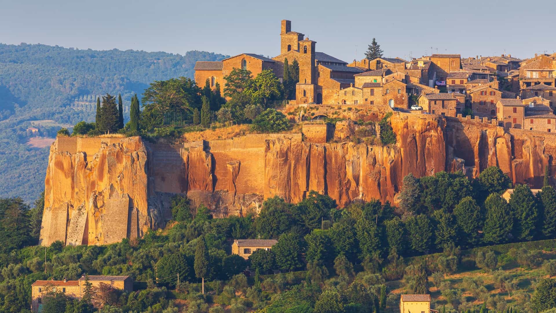 The medieval, stone-built town of Orvieto sits atop a towering, sheer, orange-colored tuff cliff overlooking a green valley.