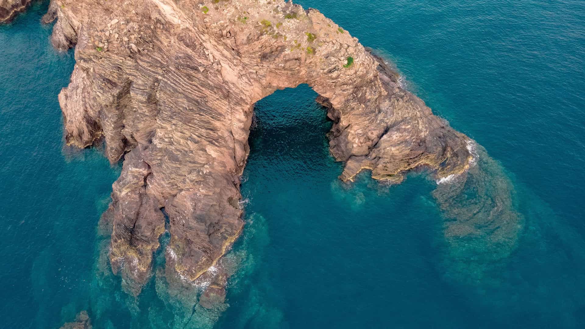 An aerial view of the Arco dell'Elefante, a large, rocky arch in the shape of an elephant, a natural landmark in Pantelleria, Italy.