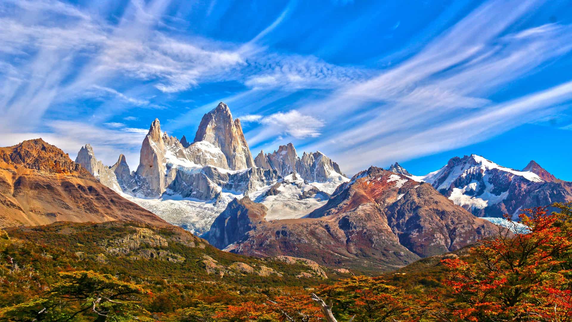 "A wide-angle landscape shot of the rugged Fitz Roy Massif in Patagonia, Argentina, with towering snow-capped peaks against a bright blue sky.  "