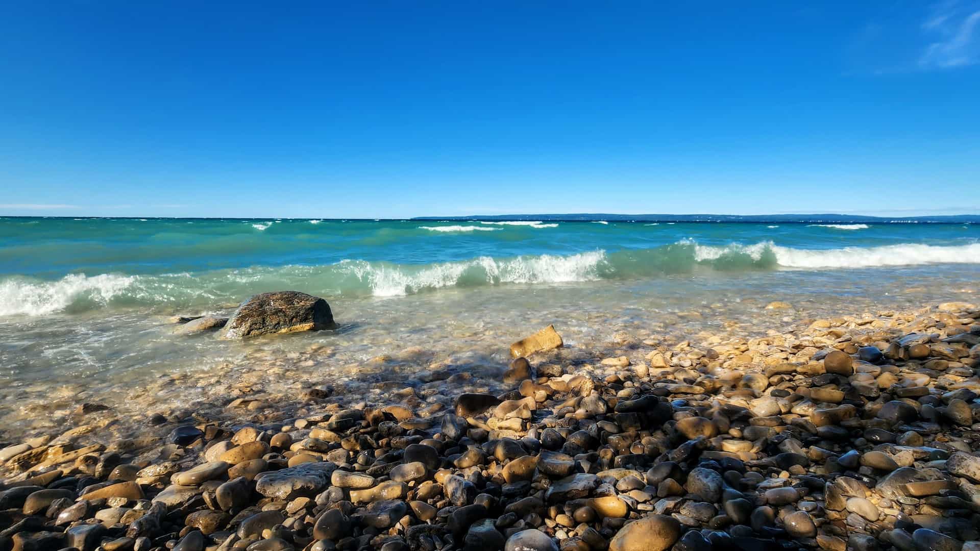 "A stunning low-angle shot of the clear blue waters of Little Traverse Bay, with small waves hitting the rocky shoreline near Petoskey, Michigan.  "