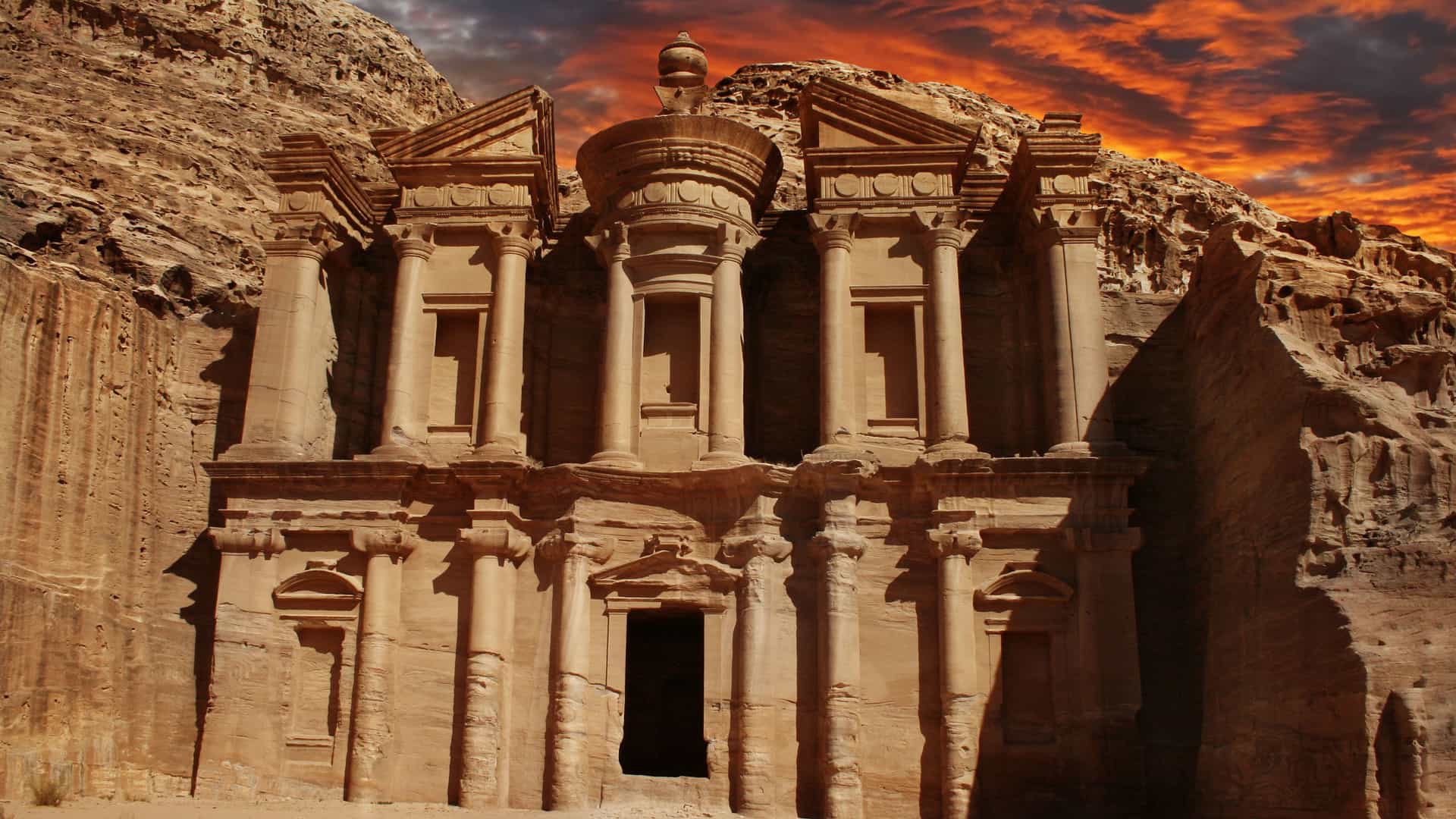 A stunning sunset view of the Ad-Dayr Monastery, a massive ancient tomb carved into a rock face, a historical landmark at the archaeological site of Petra, Jordan.