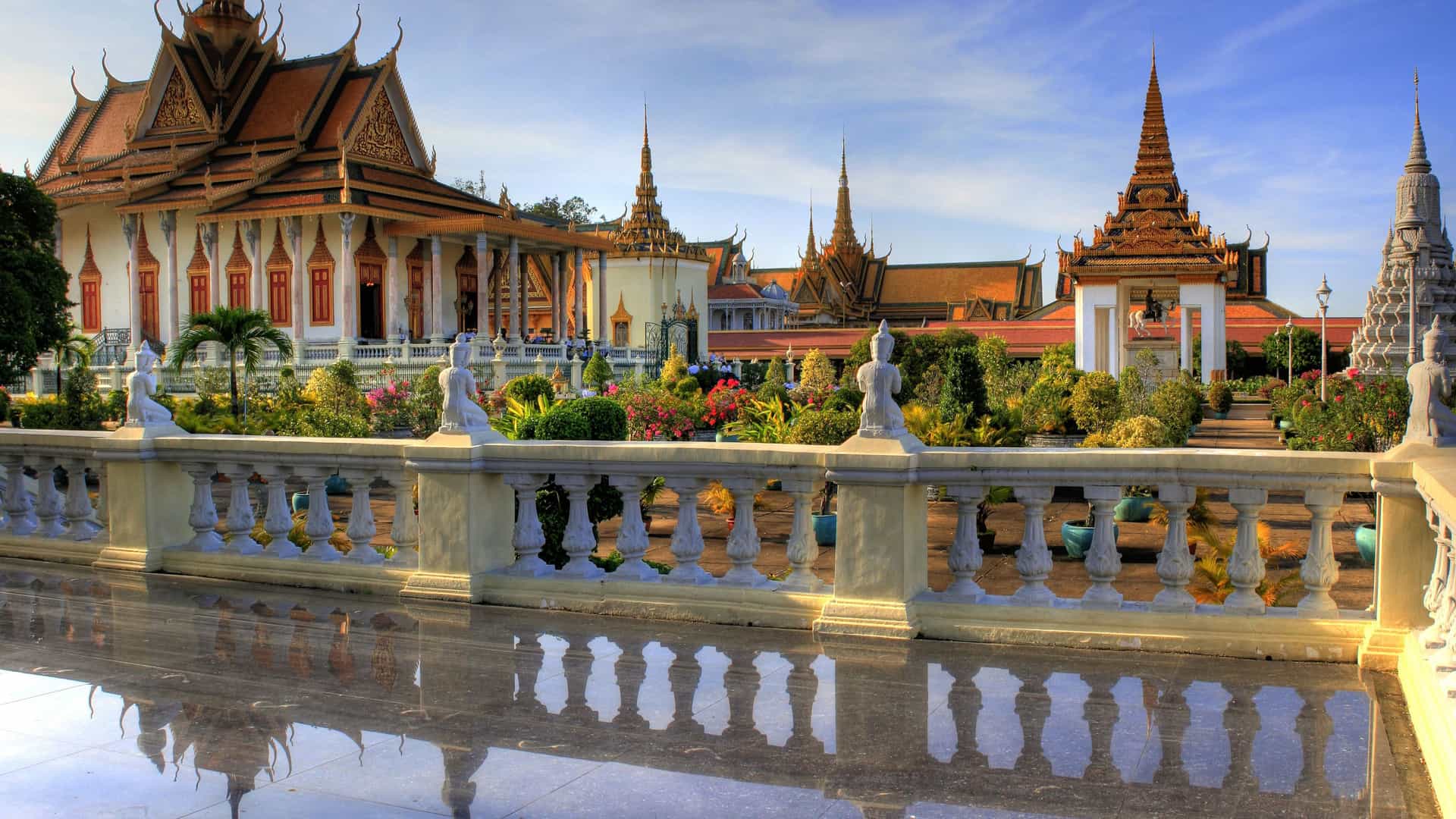 A stunning view of the Royal Palace of Phnom Penh, a historical landmark in Cambodia, with beautiful buildings, gardens, and statues under a blue sky.