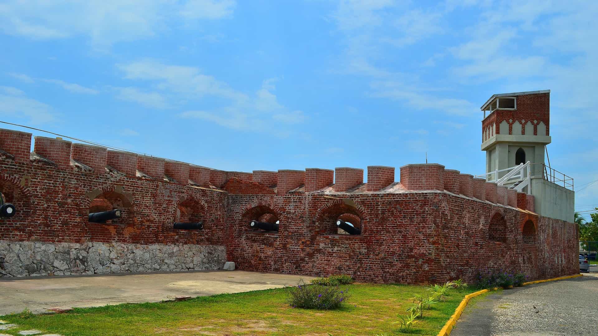 A side view of Fort Charles in Port Royal, Jamaica, a historic brick fortress with cannons protruding from its walls, under a bright blue sky.