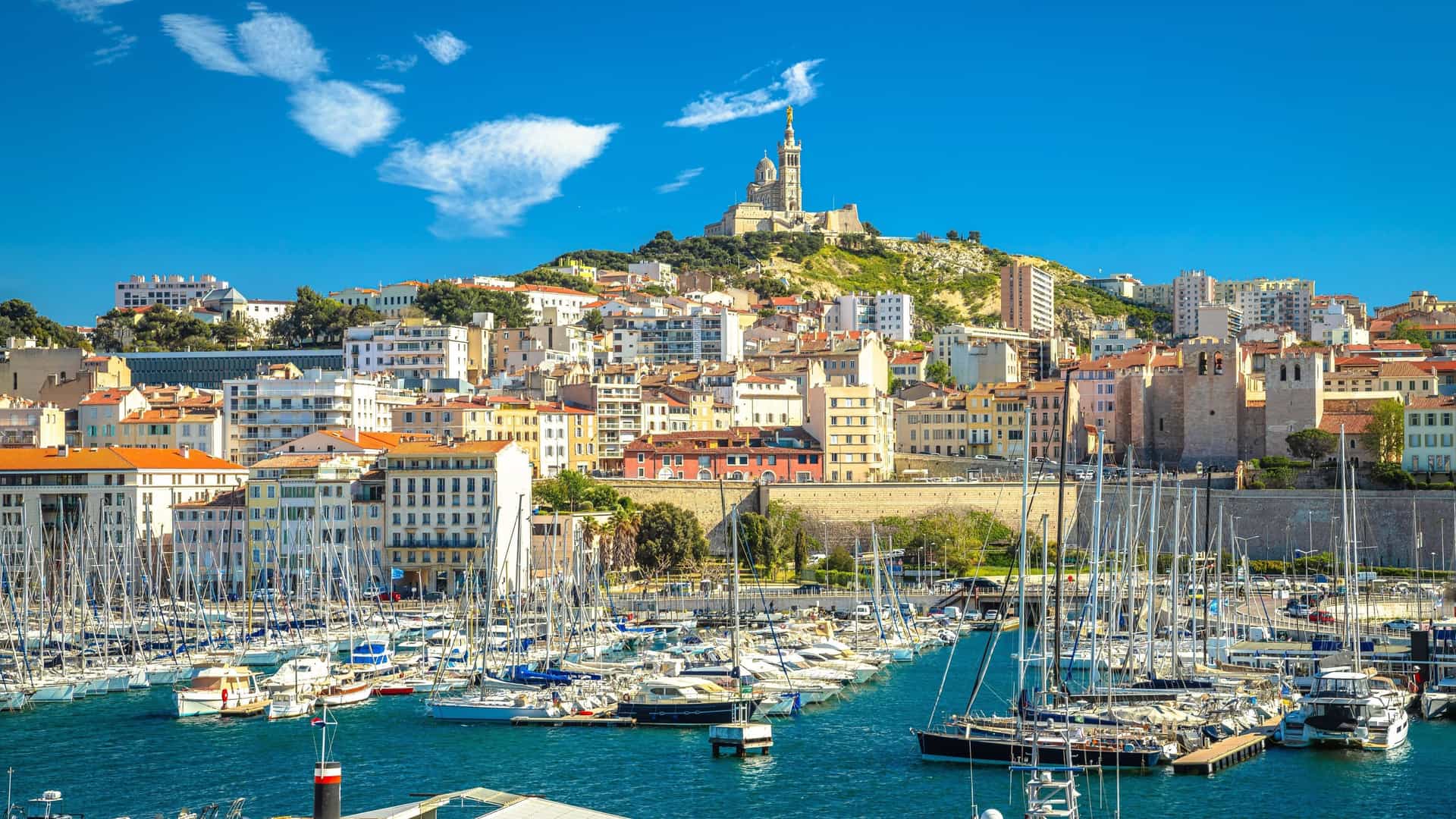 A stunning view of the Old Port of Marseille, Provence, featuring the basilica of Notre-Dame de la Garde perched on a hill overlooking the harbor filled with many yachts.