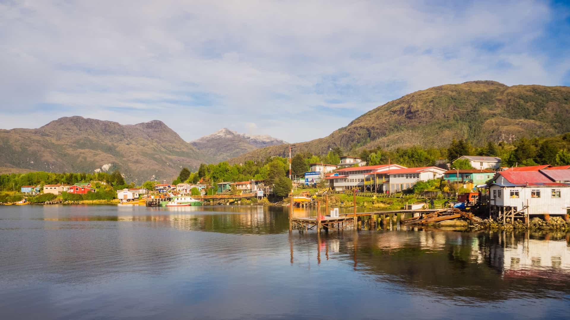 Colorful houses and wooden docks line the calm waters of the settlement of Puerto Edén, Chile, nestled among green mountains.