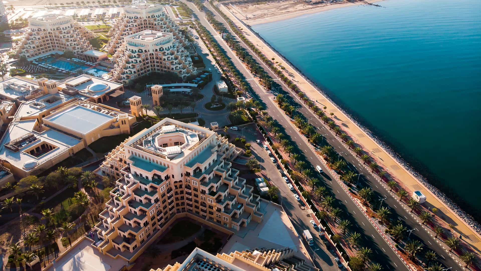 An aerial view of the Atlantis, The Palm resort complex in Dubai, featuring unique, terraced architecture and a beachfront highway along the Persian Gulf.