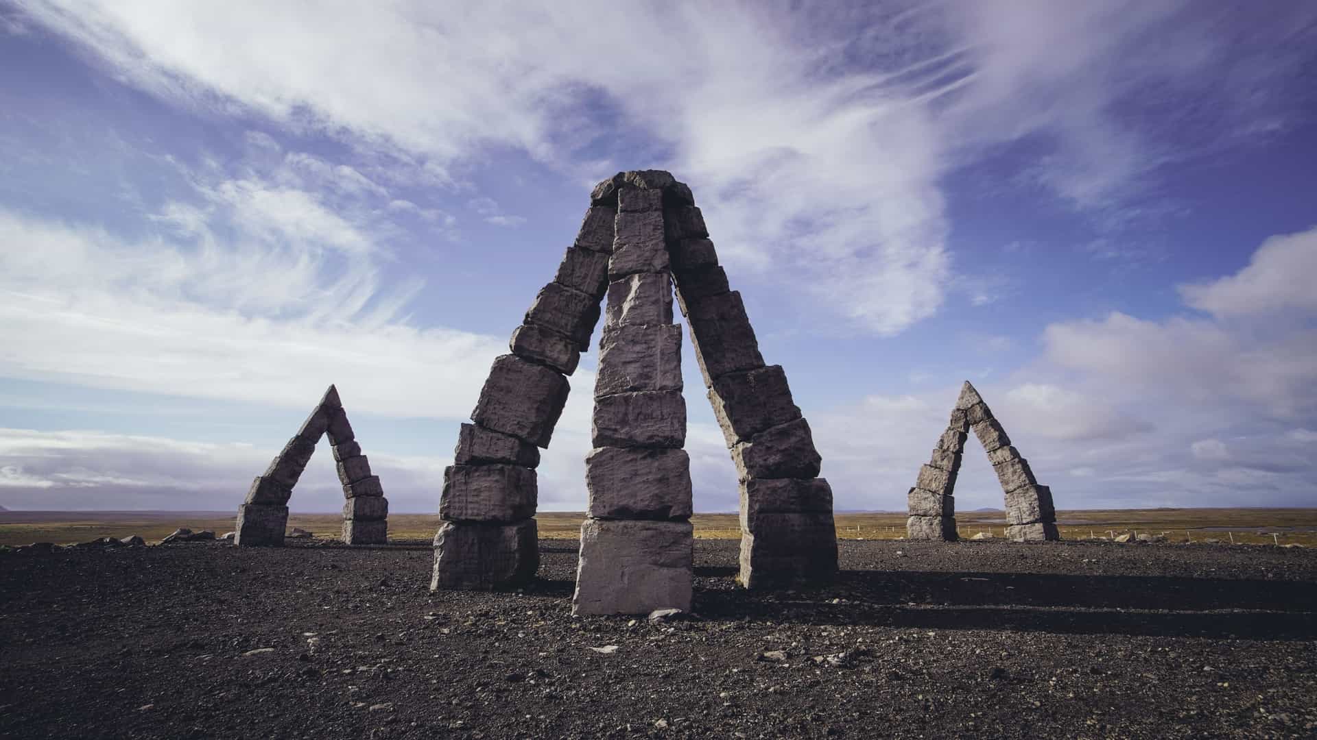The Arctic Henge in Raufarhofn, Iceland, a large stone monument with archways resembling a giant compass or sundial, set against a vast open landscape and dramatic cloudy sky.