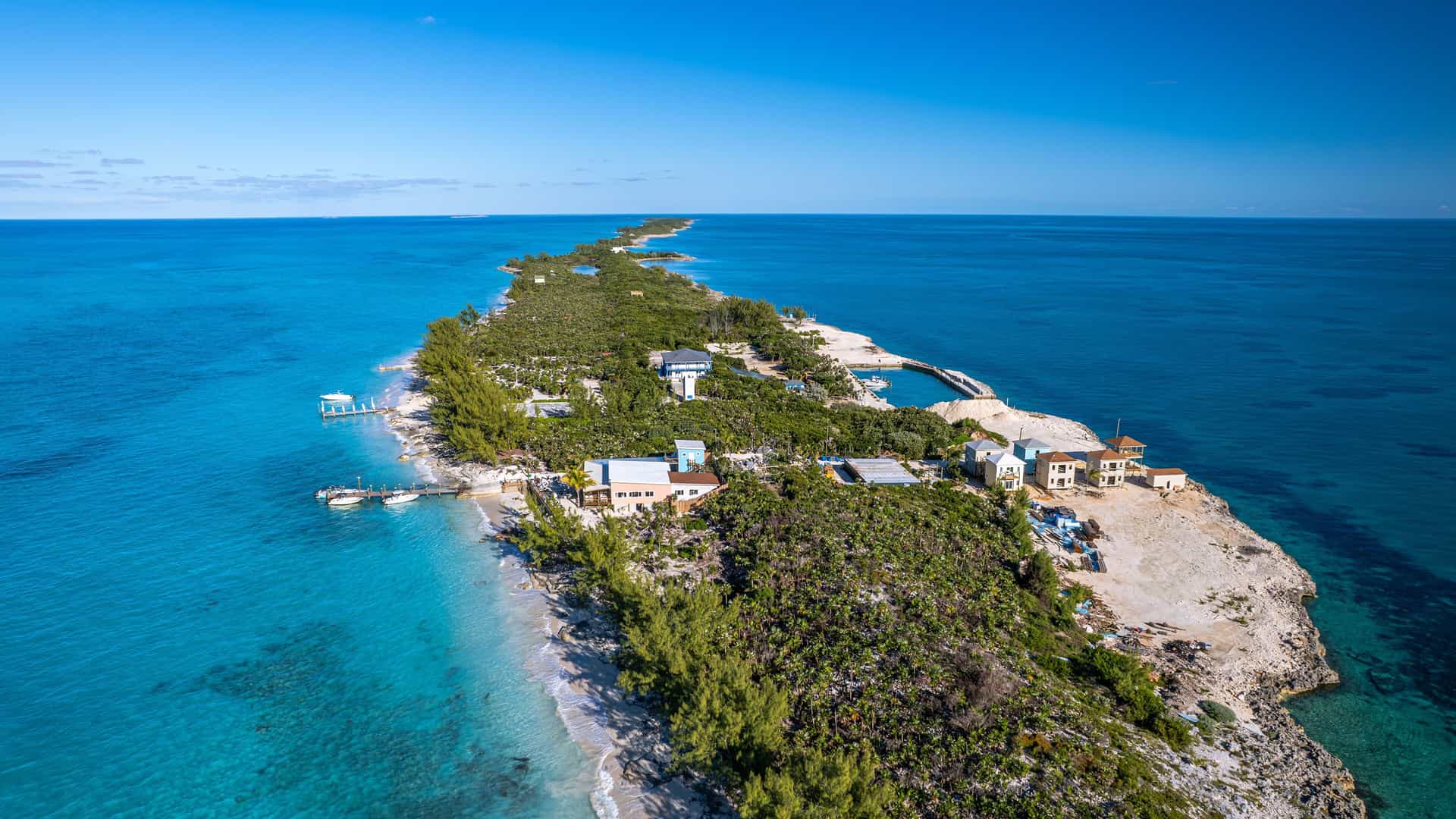 An aerial view of the long, narrow Rose Island in the Bahamas, with beautiful private beaches, resorts, and lush green vegetation surrounded by stunning clear turquoise waters.