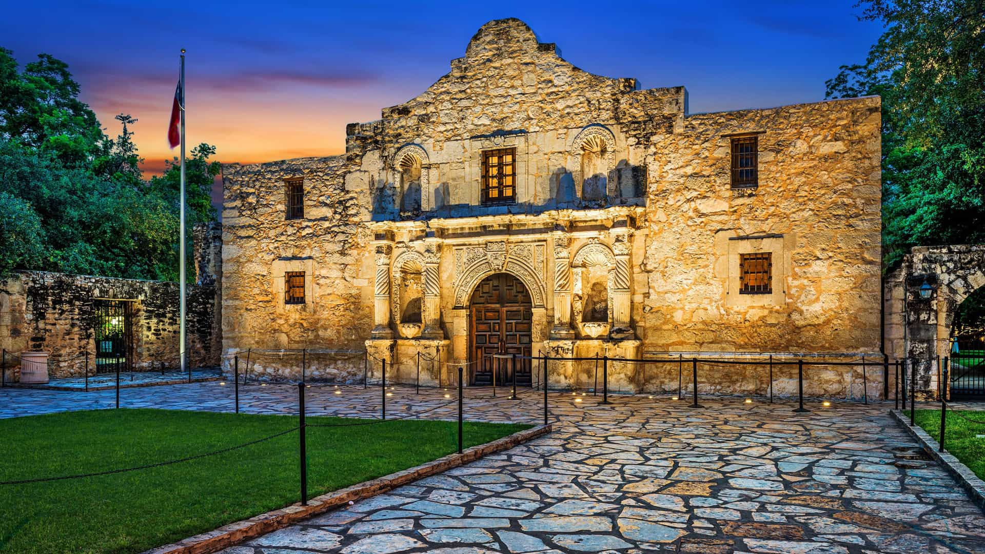 "A stunning dusk shot of the historic Alamo Mission in San Antonio, Texas, illuminated with warm lights against a dramatic blue sky."
