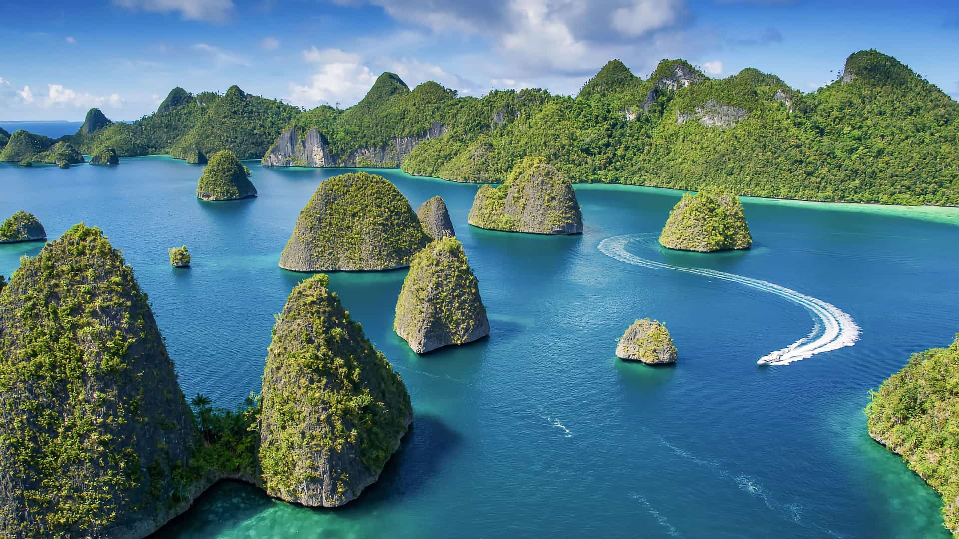 A beautiful aerial shot of Sebakor Bay, Raja Ampat, Indonesia, showcasing numerous small, lush green limestone islands surrounded by crystal-clear turquoise water and a speed boat leaving a trail behind it.