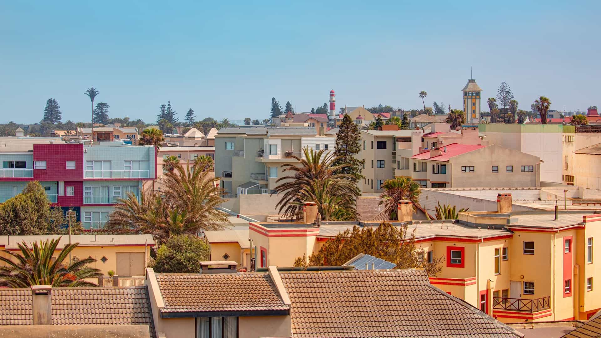 An elevated view of low-rise stucco buildings and palm trees in the coastal town of Swakopmund under a clear blue sky.