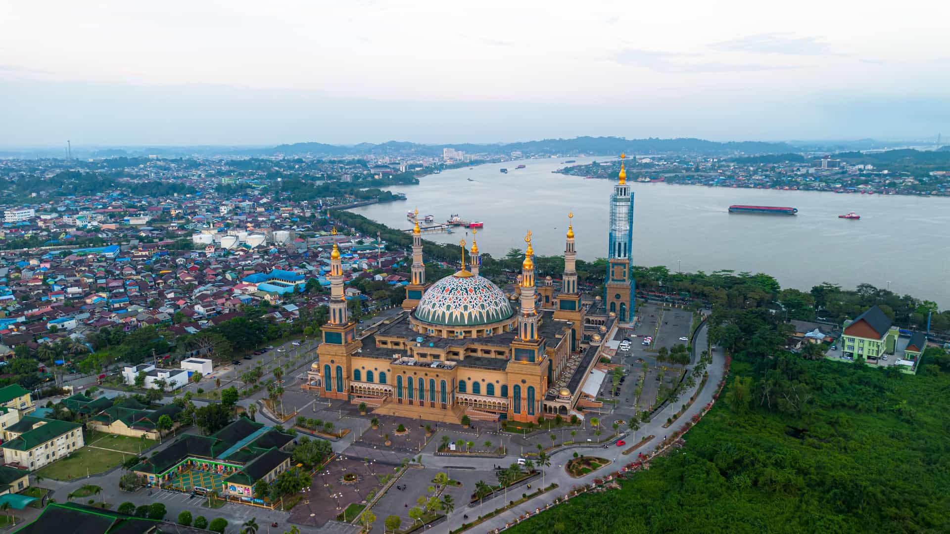 An aerial view of the majestic Masjid Islamic Centre in Tanjung Mannguar, Indonesia, with its grand domes and minarets situated along the Mahakam River.