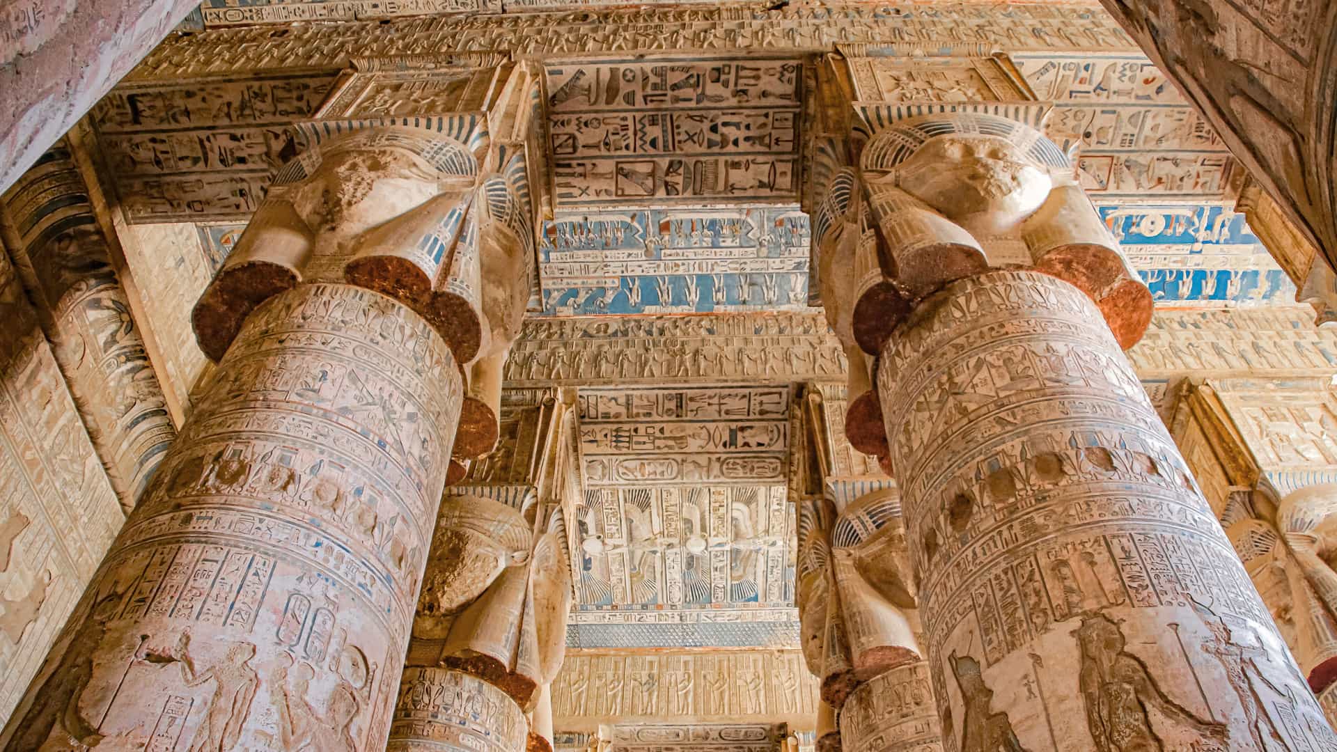 A stunning interior shot of the Temple of Hathor in Dendera, Egypt, with its intricately carved and painted columns depicting the goddess Hathor and a beautifully decorated ceiling with hieroglyphics.