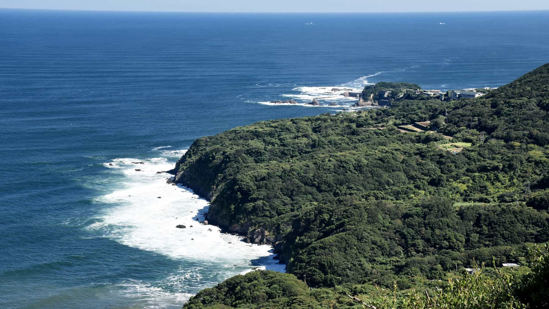 A beautiful aerial view of the rugged coastline of Toba, Japan, with green forested cliffs meeting the deep blue ocean.