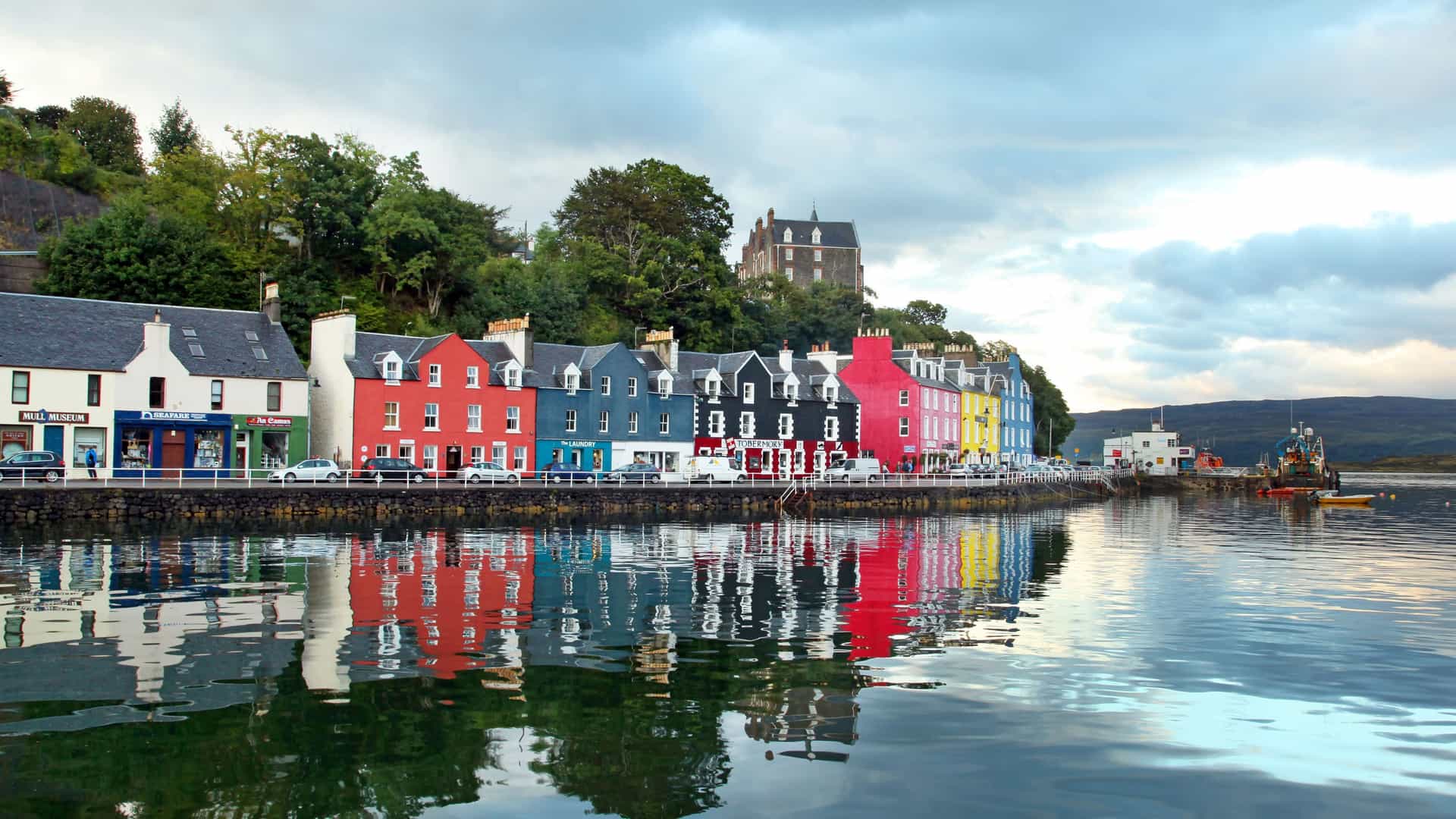 A row of brightly painted buildings on the waterfront of Tobermory, Scotland, with a historic castle perched on a hill in the background.