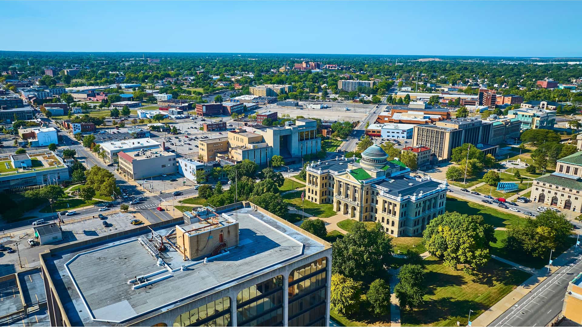 An aerial view of downtown Toledo, Ohio, featuring the historic Lucas County Courthouse and a mix of modern and traditional buildings in the urban landscape.