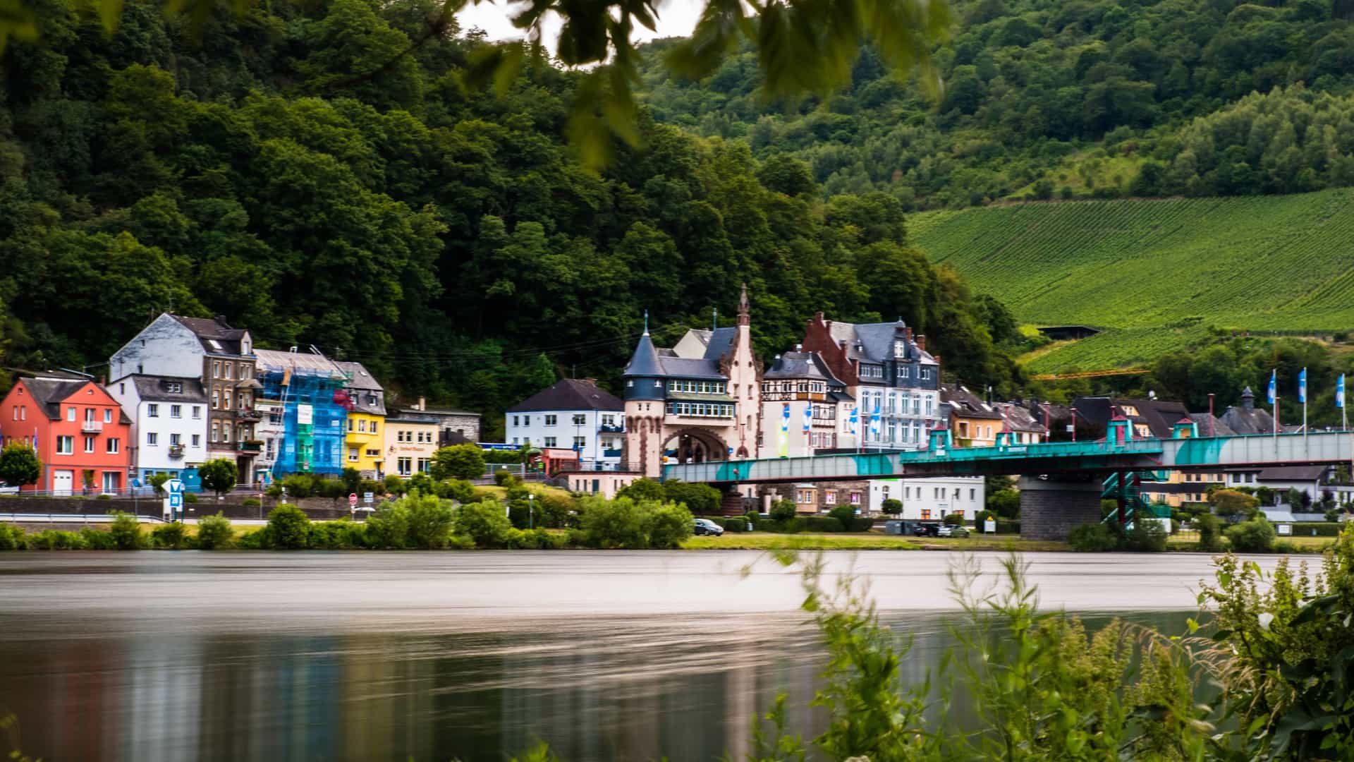 A charming view of the town of Traben-Trarbach in Germany, with colorful buildings along the Mosel River and green, terraced vineyards on the hills.