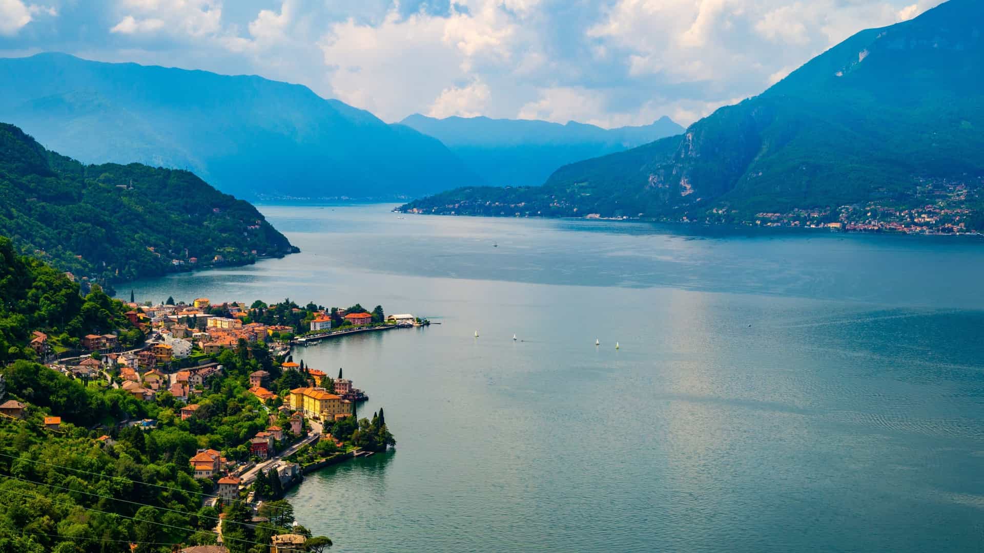 The colorful town of Tremezzina is nestled on the shore of Lake Como, backed by enormous, blue-tinged mountain ranges.
