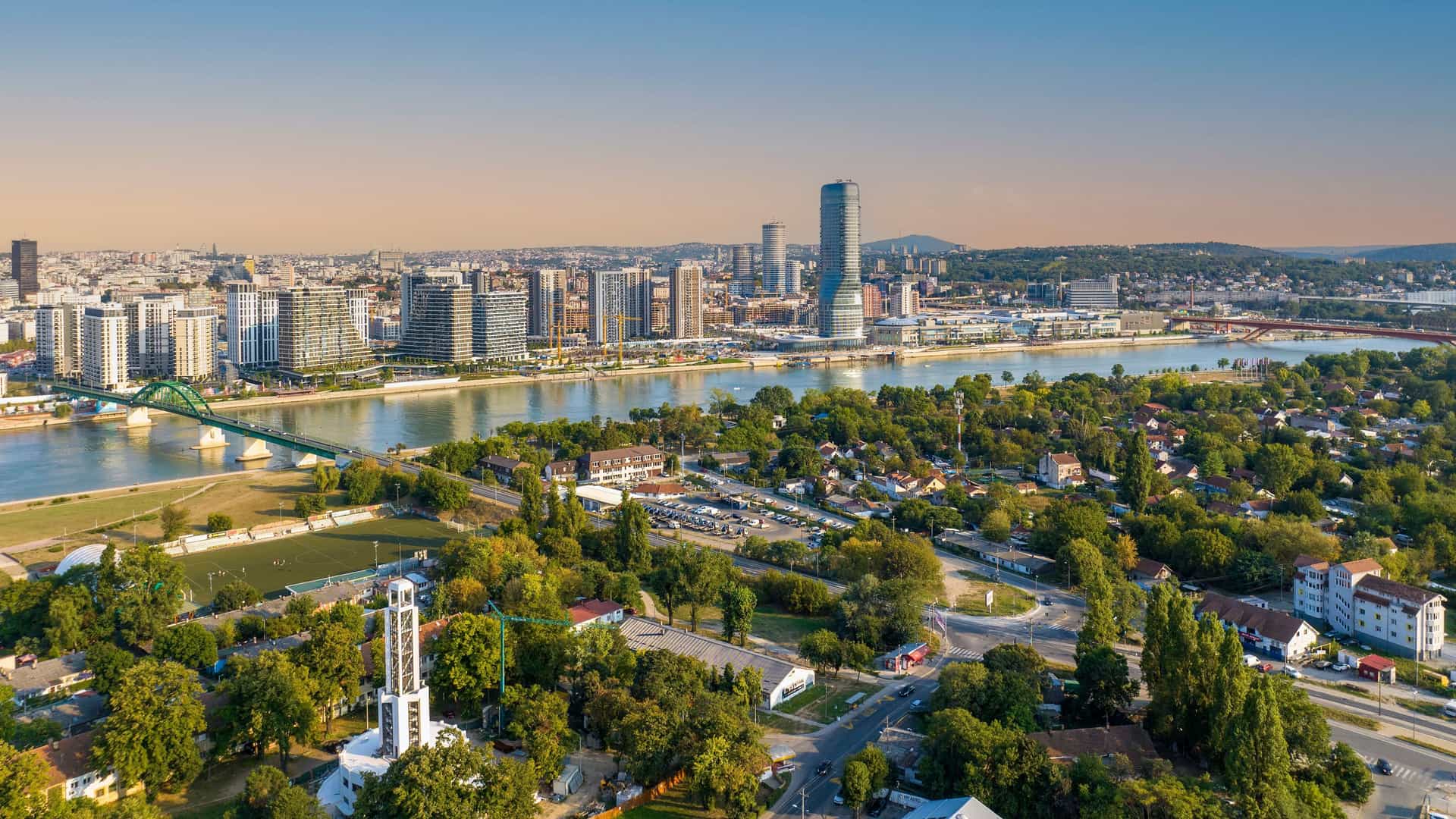 An aerial shot of Belgrade, Serbia, with the Sava River dividing the city, showing a mix of modern and historical architecture on the riverbanks.