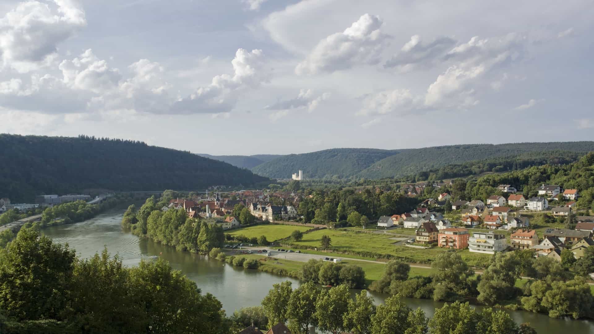 A high-angle view of the charming town of Wertheim, Germany, nestled on the banks of the Main River, surrounded by lush, green hills and a scenic valley.