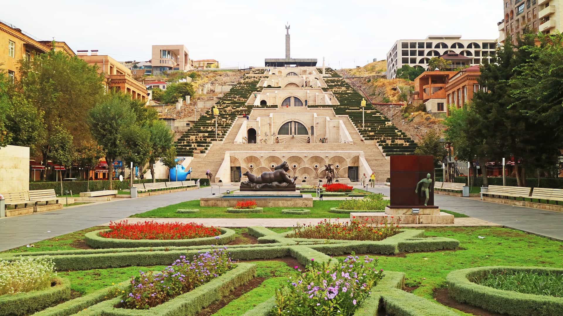 "A scenic view of the massive Yerevan Cascade complex in Armenia, with its large stone stairways, multiple levels of fountains and sculptures, and landscaped gardens in the foreground."