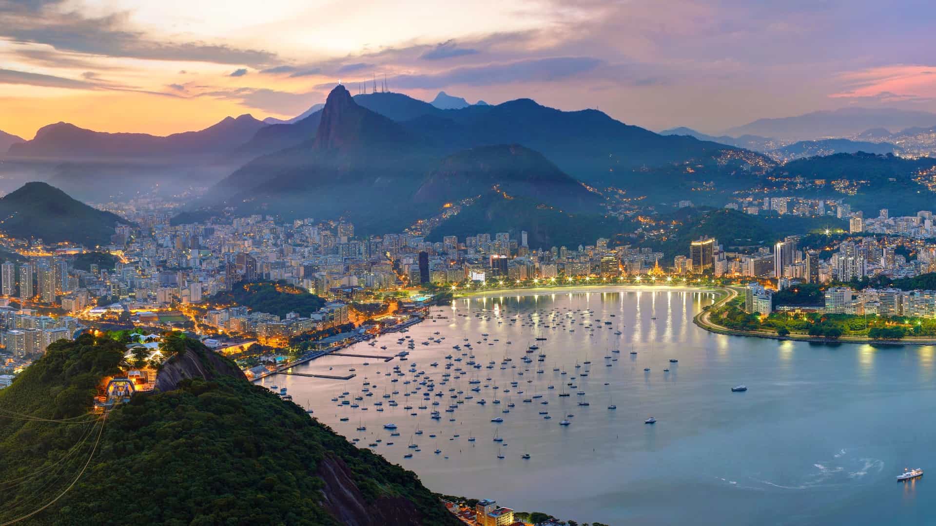 An iconic panoramic view of Rio de Janeiro, Brazil, at dusk, showcasing its illuminated bay, city lights, and dramatic mountains like Sugarloaf, a vibrant port on Princess Cruises' South America voyages.