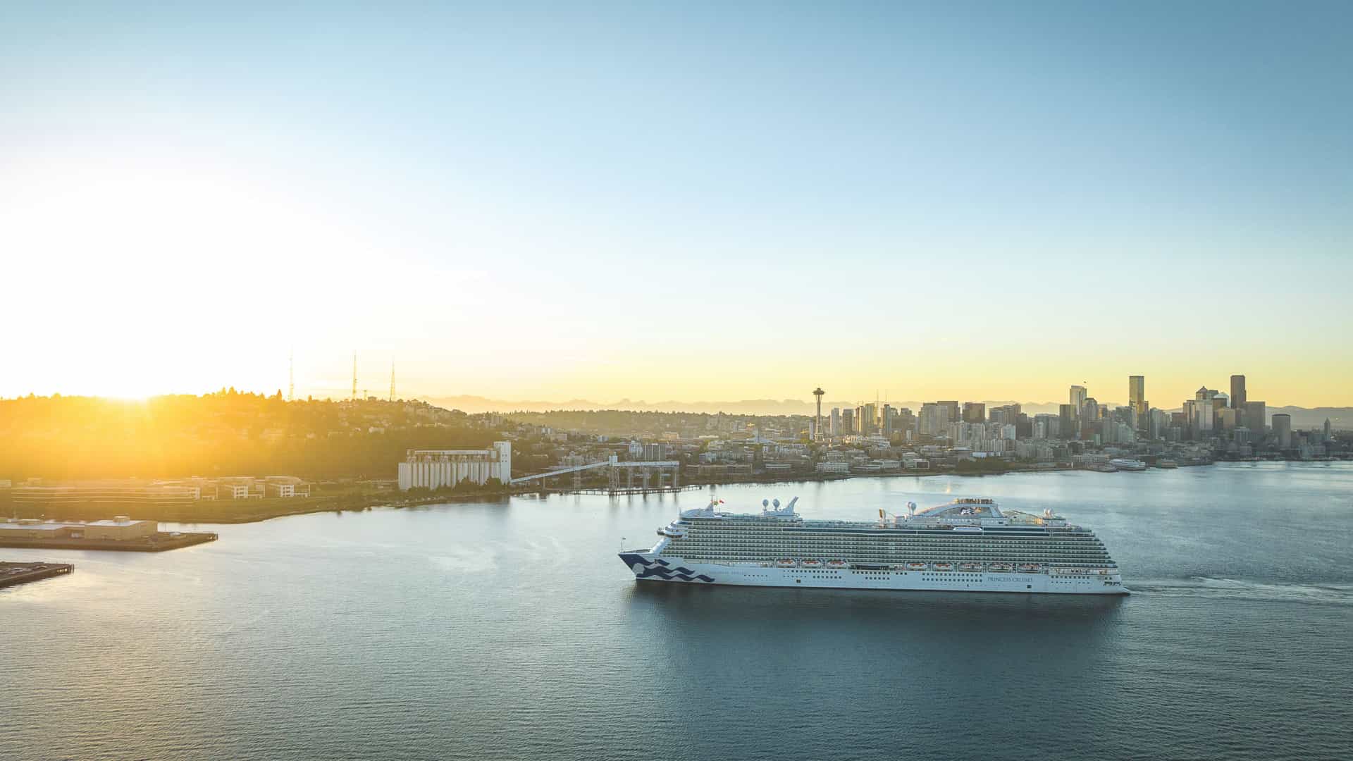 A Princess Cruises ship sails in front of the Seattle skyline with the Space Needle during a vibrant sunset, showcasing a potential departure point for a Transpacific cruise.