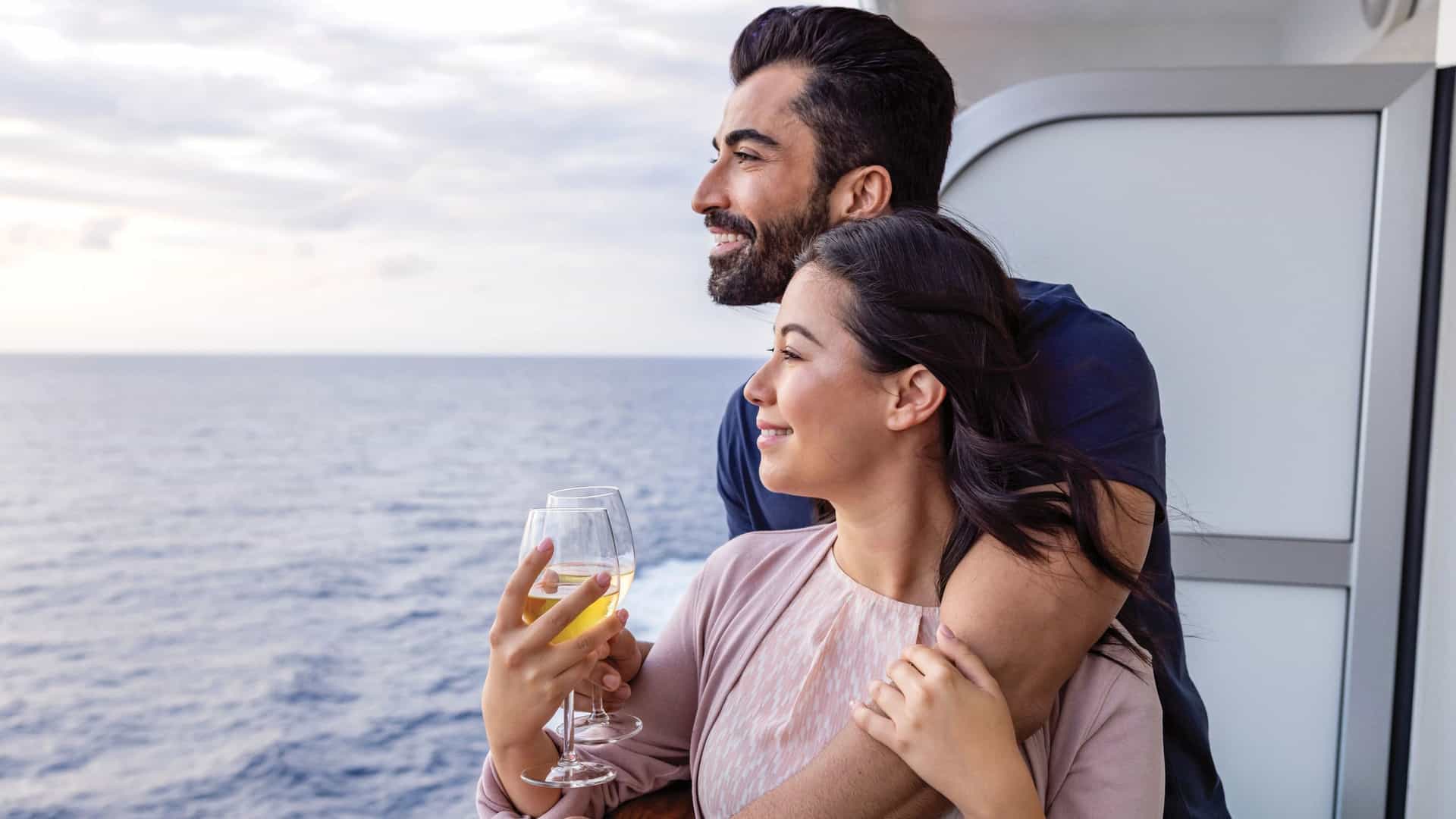 A happy couple enjoys a drink on their balcony stateroom aboard a Princess Cruises ship, gazing out at the vast ocean, emblematic of a World Cruise experience.