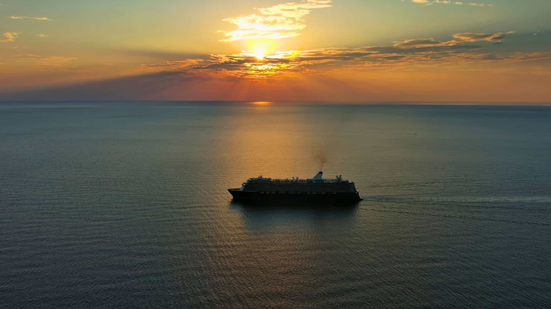 A private charter cruise sails across the ocean during a vibrant sunset, casting warm colors on the water.