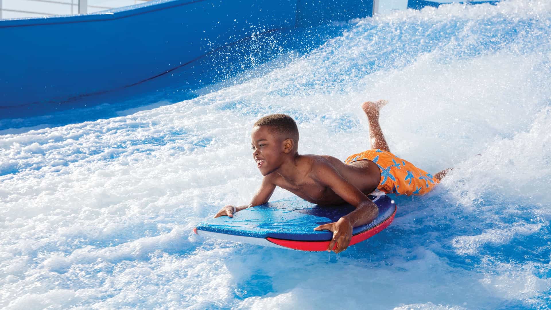 A young boy balances on a surfboard as he rides a wave on Royal Caribbean's FlowRider.