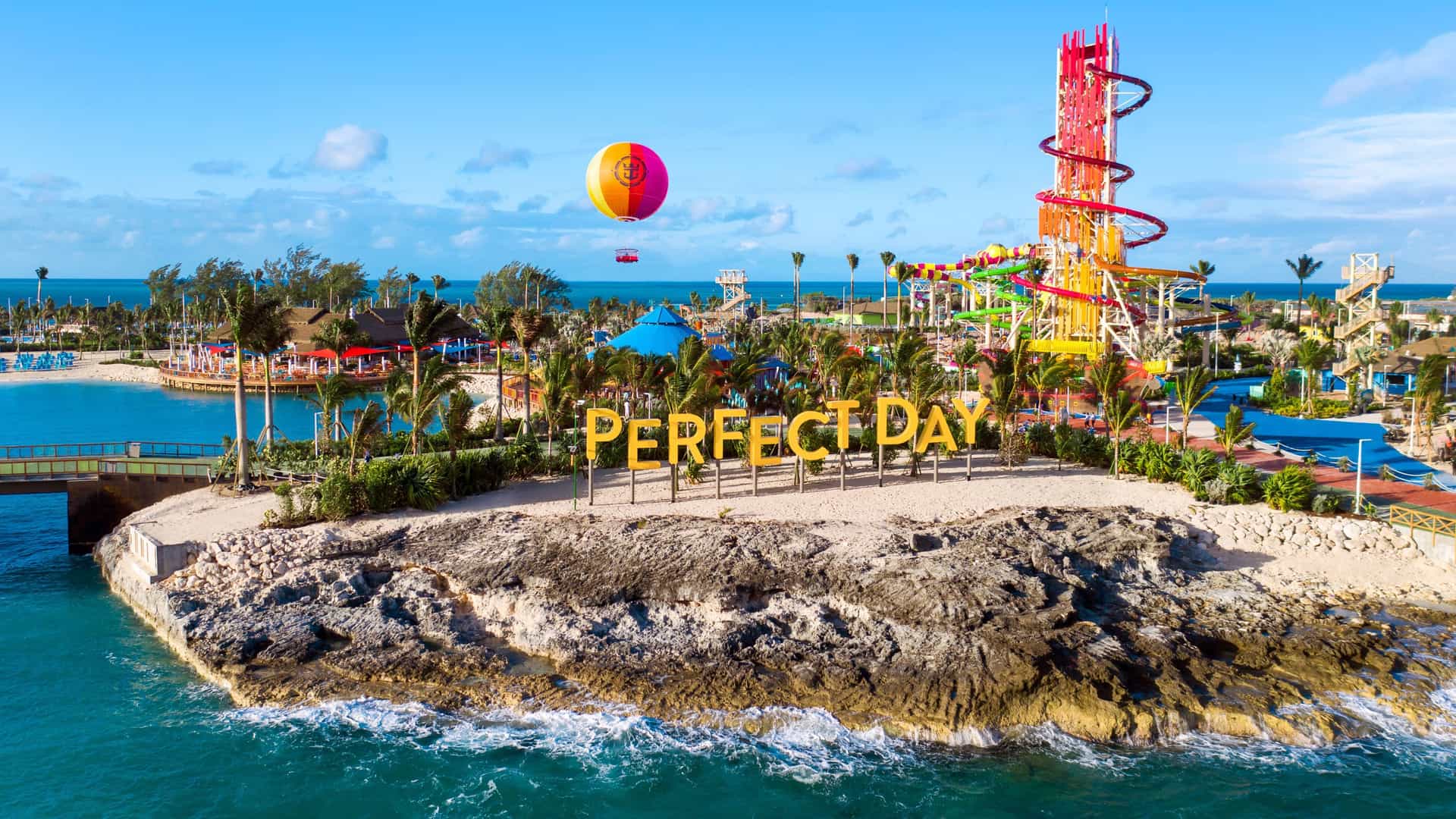 An aerial view of Royal Caribbean's Perfect Day at CocoCay in The Bahamas, showcasing the iconic Thrill Waterpark and a hot air balloon floating above the pristine beach.