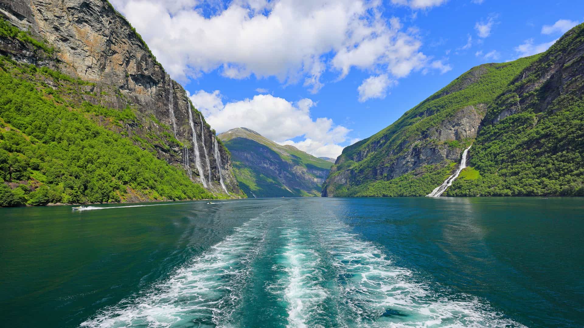 A spectacular view of Geirangerfjord, Norway, from the wake of a Seabourn cruise ship, highlighting the majestic mountains and waterfalls of Northern Europe.